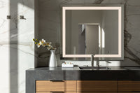 Bathroom vanity with a black countertop, wood drawers, and a backlit mirror against a marble wall.

