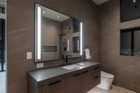 Modern bathroom with a dark vanity, stone walls, a mirror with lights on each side, and a wall-mounted toilet.

