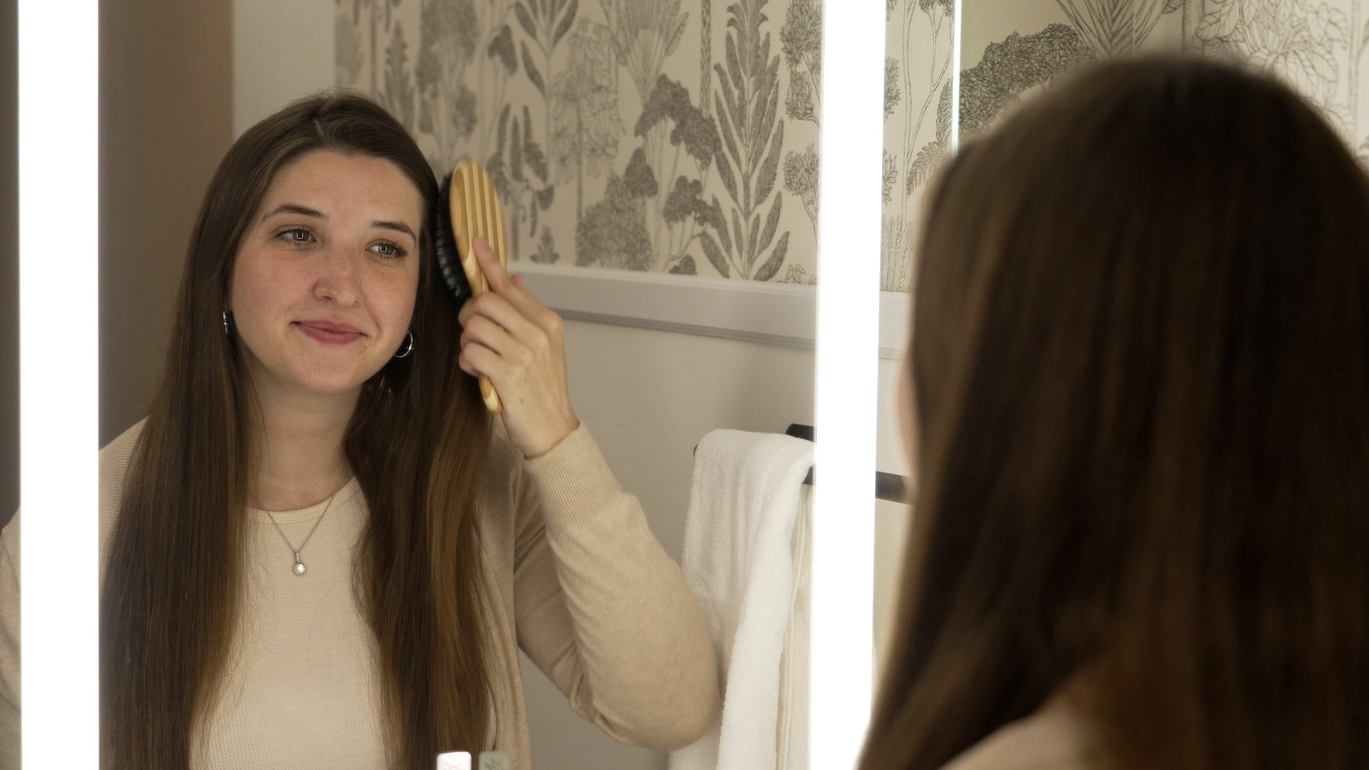 Load video: young woman brushing her hair while using a lighted mirror