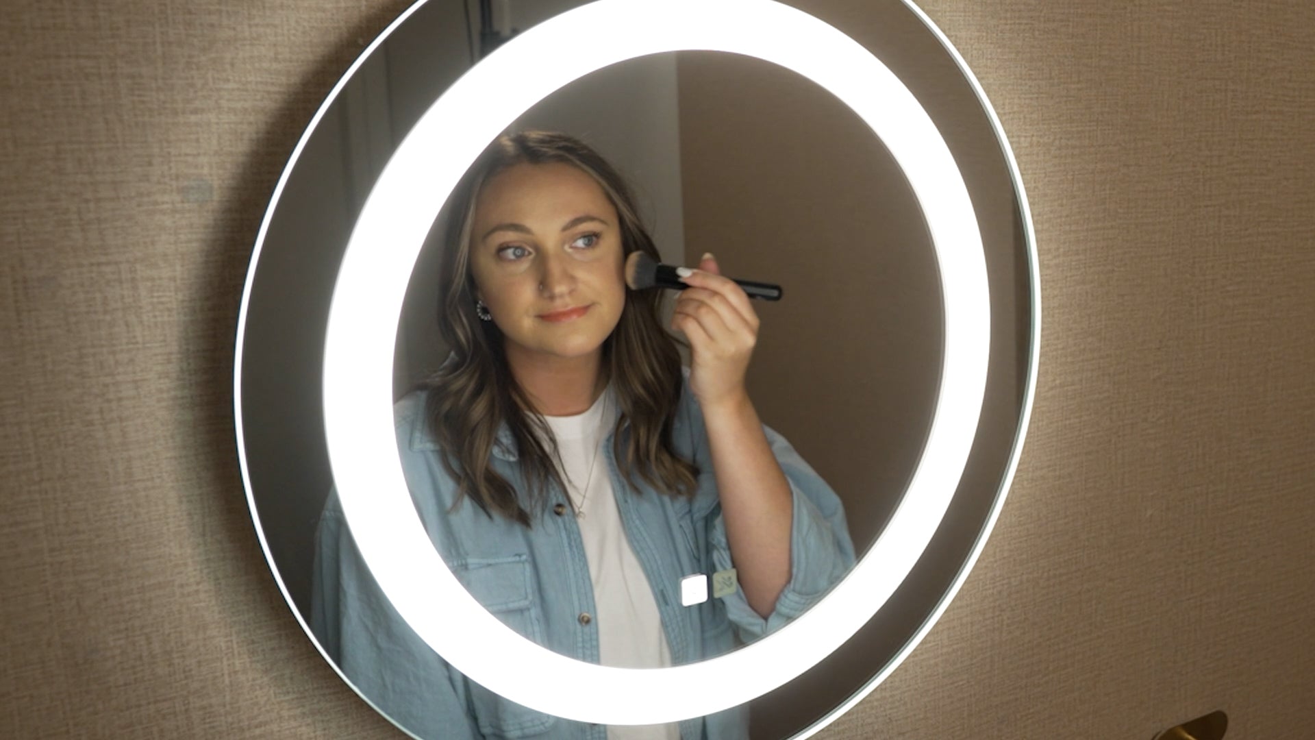 Load video: Woman applying makeup in a round lighted mirror