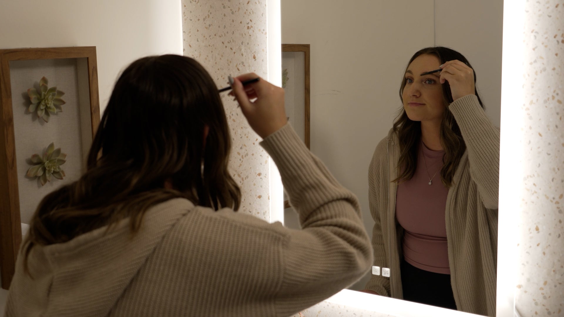 Load video: Woman applying makeup using a backlit lighted mirror in a bathroom